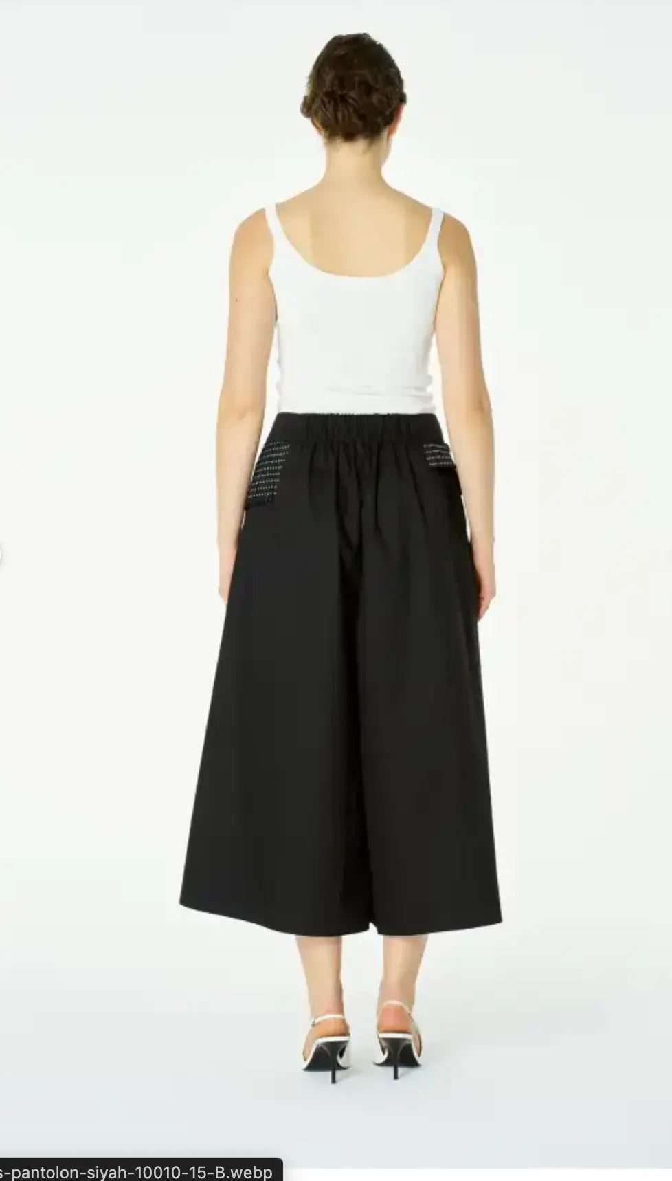 Person wearing a white tank top and black wide-leg pants on a white background