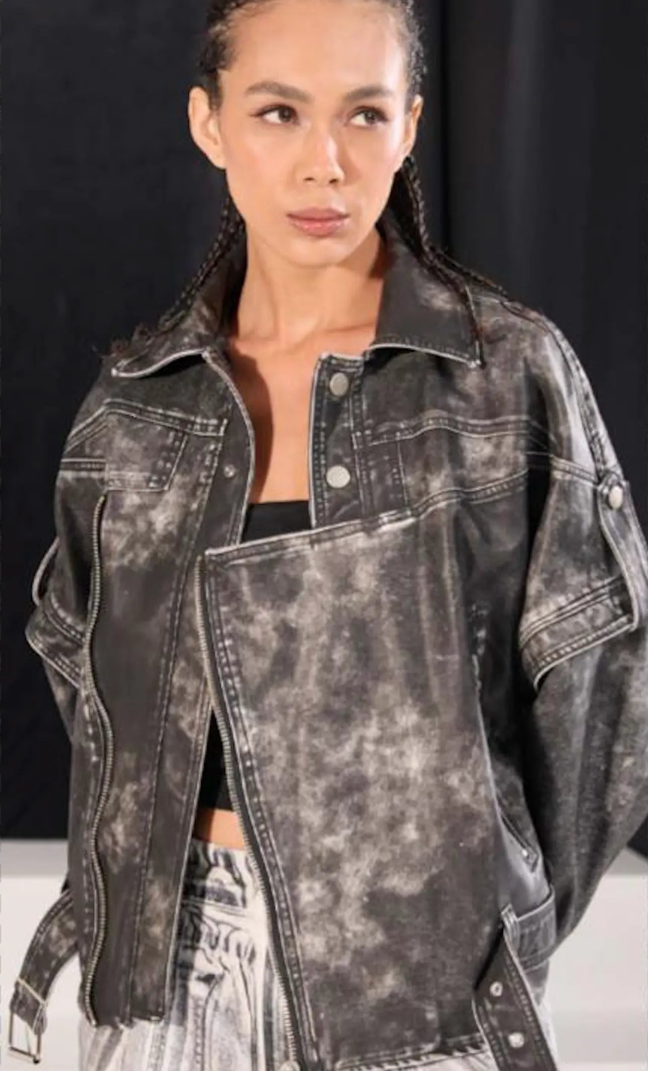 Person wearing a distressed black denim jacket against a dark background