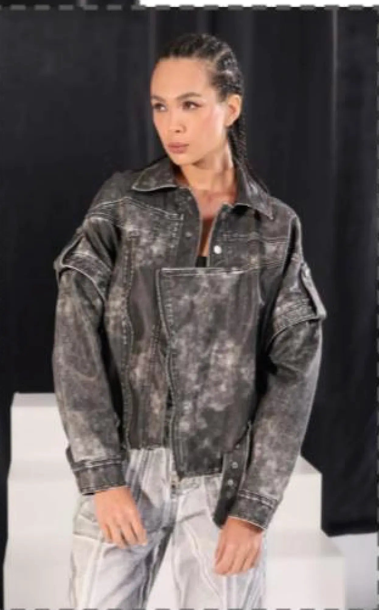 Person wearing a distressed denim jacket against a black background