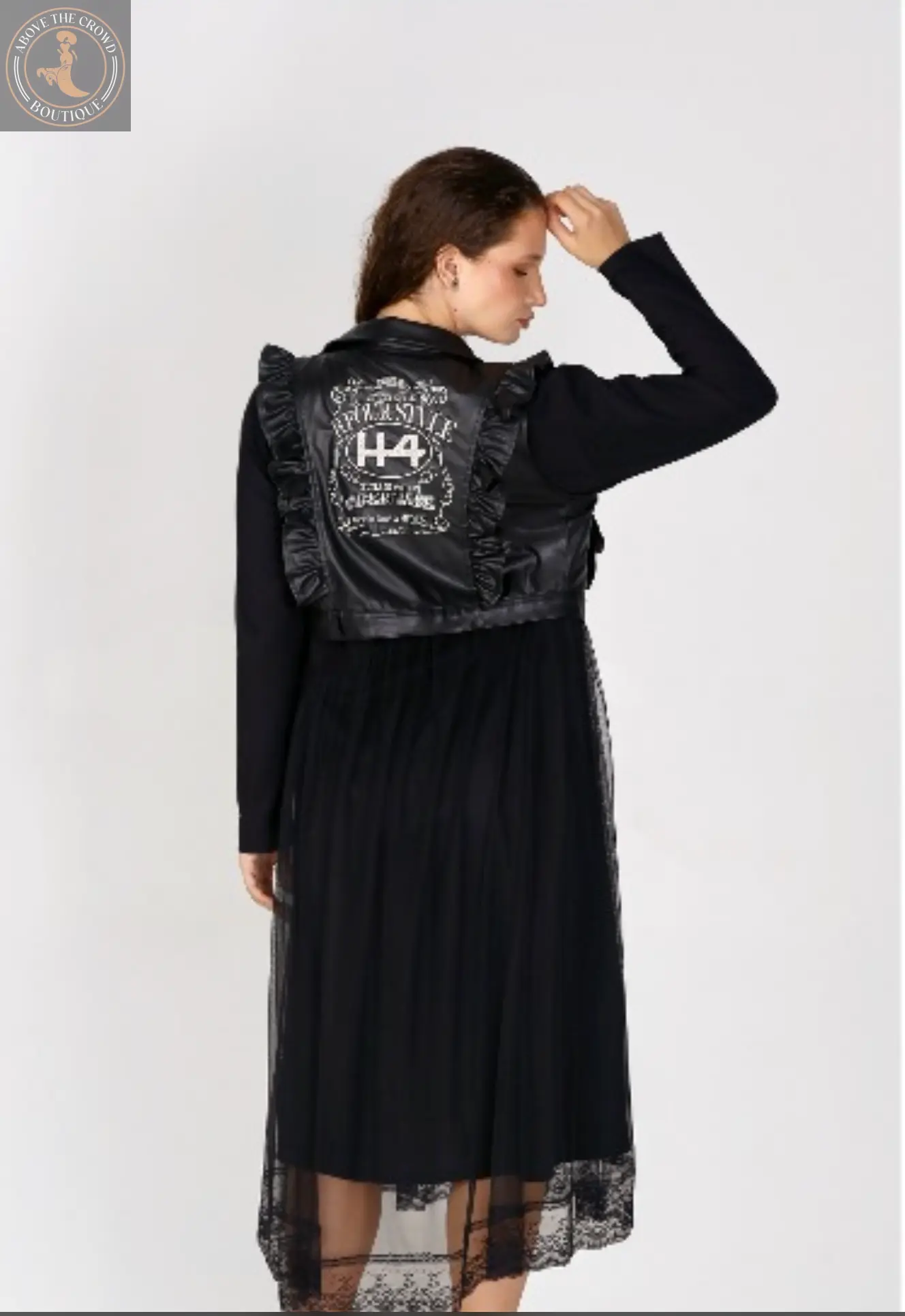 Person wearing a black dress with lace details and a jacket with text on the back against a white background
